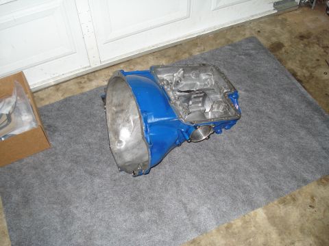 1984 Ford Bronco - A blue transmission housing sits on a mat in a garage, with a box of parts nearby.