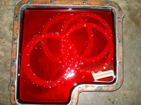 1984 Ford Bronco - Transmission pan contains red fluid with visible metal shavings and clutch plates, indicating internal wear.
