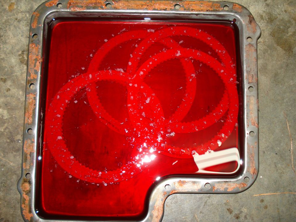 Transmission pan filled with red fluid, showing metal shavings and clutch plates