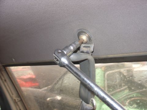 1988 Ford Bronco - A socket wrench is used to remove a bolt from the vehicle's headliner, with other vehicles seen through the window.