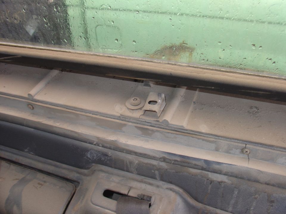 Close-up of a metal bracket and screw on the interior trim near a dusty window