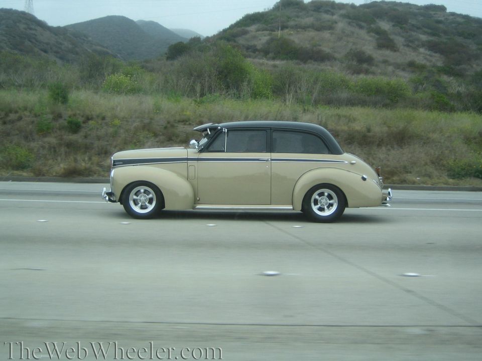 Tan 1940s convertible street rod with black top on a freeway