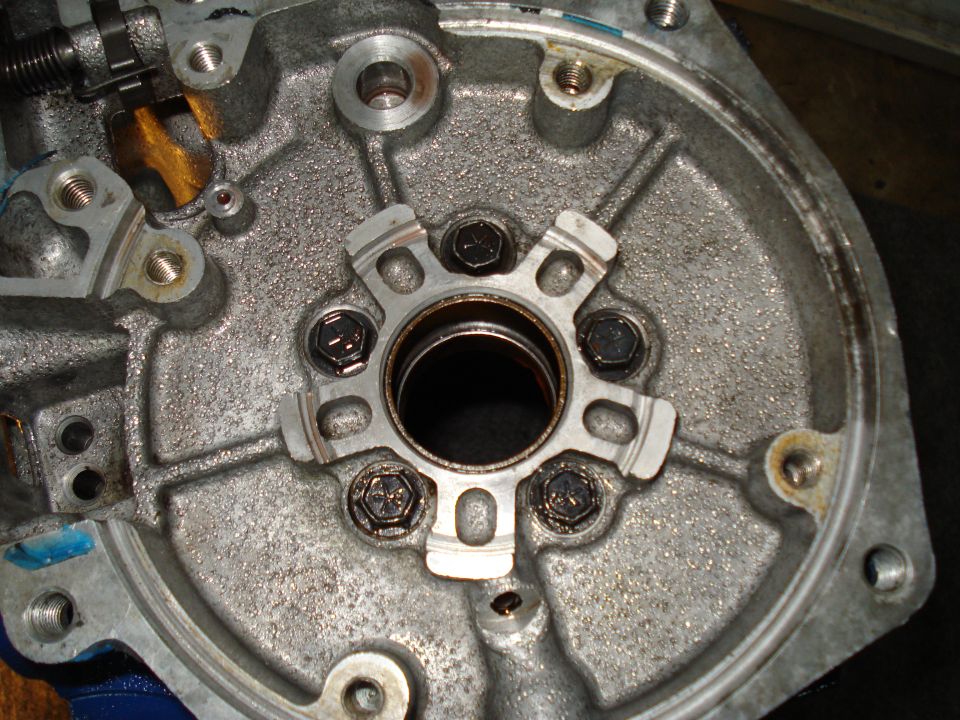 Metal transmission housing with bolts and a central opening. Some oil residue is visible