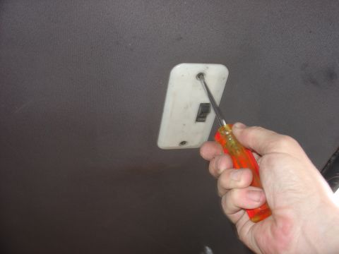 1988 Ford Bronco - A screwdriver is used to remove a light fixture from the vehicle's headliner.