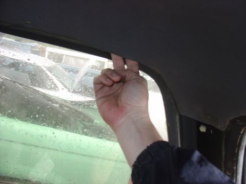 1988 Ford Bronco - A hand reaches for the headliner near the window frame of an older vehicle, with other vehicles visible through the window.