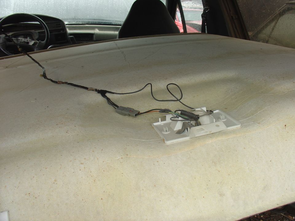 Interior shot of a car's headliner with exposed wiring and a light fixture. Dashboard and steering wheel visible
