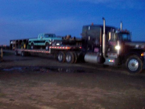 1994 Ford F-150 - A light blue pickup truck is transported on a flatbed trailer behind a large semi-truck at dusk.