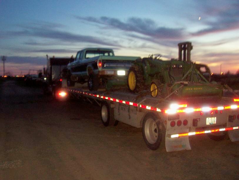 Ford pickup truck and John Deere tractor on a flatbed trailer at dusk