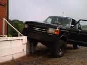 1990 Ford Bronco - Black 1992 Ford F-150 pickup truck with driver's door open, parked next to a concrete structure.