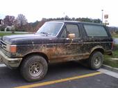 1990 Ford Bronco - Mud-covered Ford Bronco parked in a lot with trees in the background.