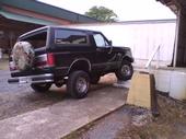 1990 Ford Bronco - This black Ford Bronco is parked outside a building with a spare tire mounted on the rear door.