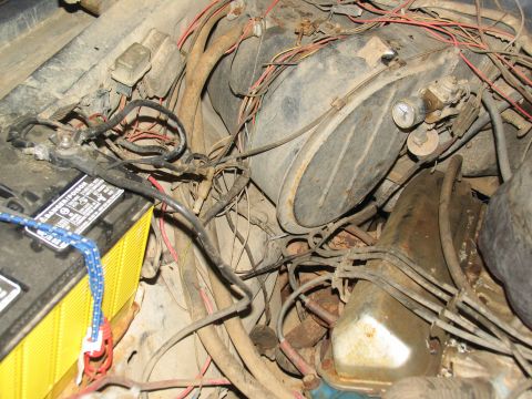 1978 Ford Bronco - The engine bay is cluttered with wires and components, showing a battery and part of the engine block.