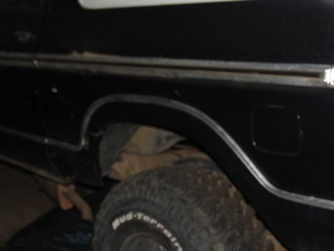1978 Ford Bronco - Rear quarter panel of a black SUV, showing chrome trim and a Mud-Terrain tire. The vehicle appears to be in a pre-restoration state.