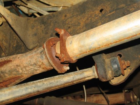 1978 Ford Bronco - Close-up view of the exhaust pipe flange and suspension components, showing significant rust on the undercarriage of a vehicle.