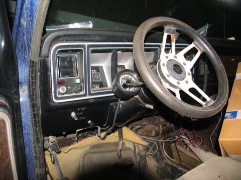 1978 Ford Bronco - The interior of an older vehicle shows a worn dashboard, steering wheel, and floor pedals, with some added gauges.