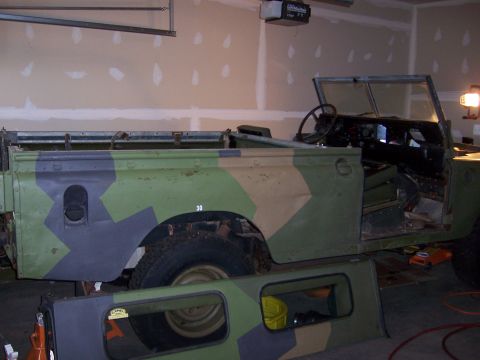 1974 Land Rover Land Rover - This Land Rover, painted in a camouflage pattern, is in a garage, likely undergoing restoration or awaiting restoration.