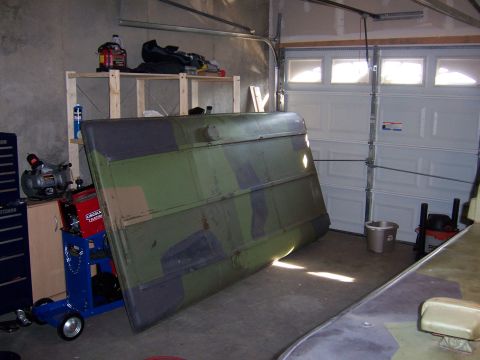 1974 Land Rover Land Rover - A large, camouflaged panel rests in a garage, leaning against a wall near a workbench and tools.