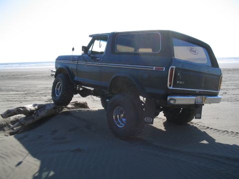 1989 Ford Bronco - A lifted 1978 Ford Bronco navigates a sandy terrain near the ocean, with its rear facing the camera.