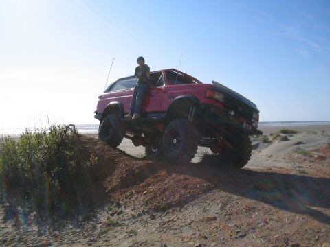 1989 Ford Bronco - A red 1989 Ford Bronco is shown lifted and positioned on a sandy incline near the ocean.