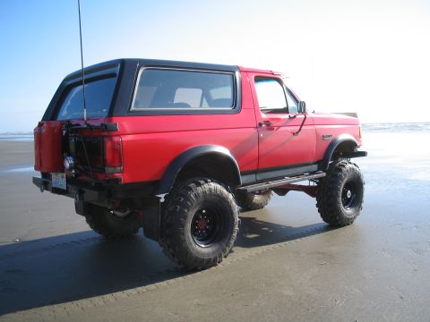 1989 Ford Bronco - Red 1989 Ford Bronco with aftermarket wheels and tires sits on a sandy beach.