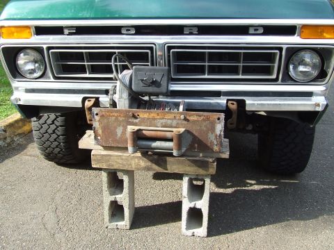 1979 Ford Bronco - The front grille and bumper of a green 1979 Ford Bronco, fitted with a winch and supported by cinder blocks.