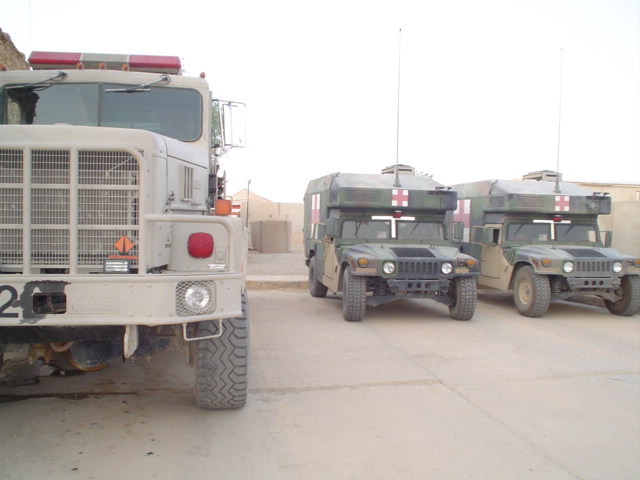 Front of a large military truck next to two Humvees with red cross markings