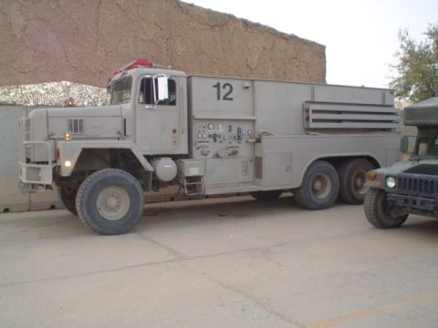 1981 Ford Bronco - A large military truck, possibly a water tender, is parked next to a Humvee in an arid environment.