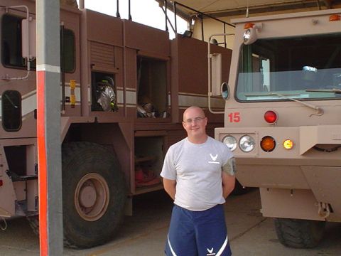 1981 Ford Bronco - A man stands in front of two large tan fire trucks parked inside a garage.