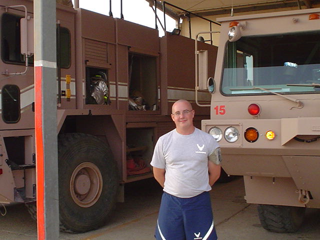 Two tan fire trucks parked side-by-side in a garage, a man stands between them