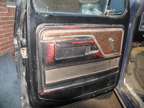 1978 Ford Bronco - Interior door panel showing wear and tear, with a woodgrain insert and manual window crank.