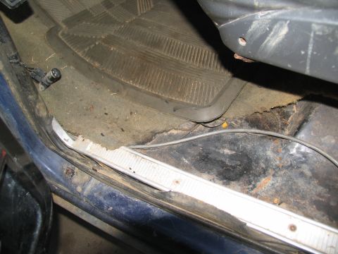 1978 Ford Bronco - The interior floor of the vehicle shows significant wear and tear, with a rubber mat over carpet and visible rust on the metal.