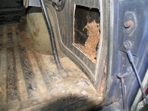 1978 Ford Bronco - The interior of a vehicle shows significant damage to the door panel and rust on the floor.