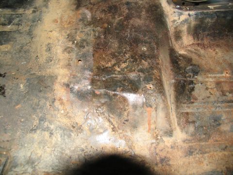 1978 Ford Bronco - The interior floor pan of a vehicle shows significant rust and dirt, with evidence of past repairs.
