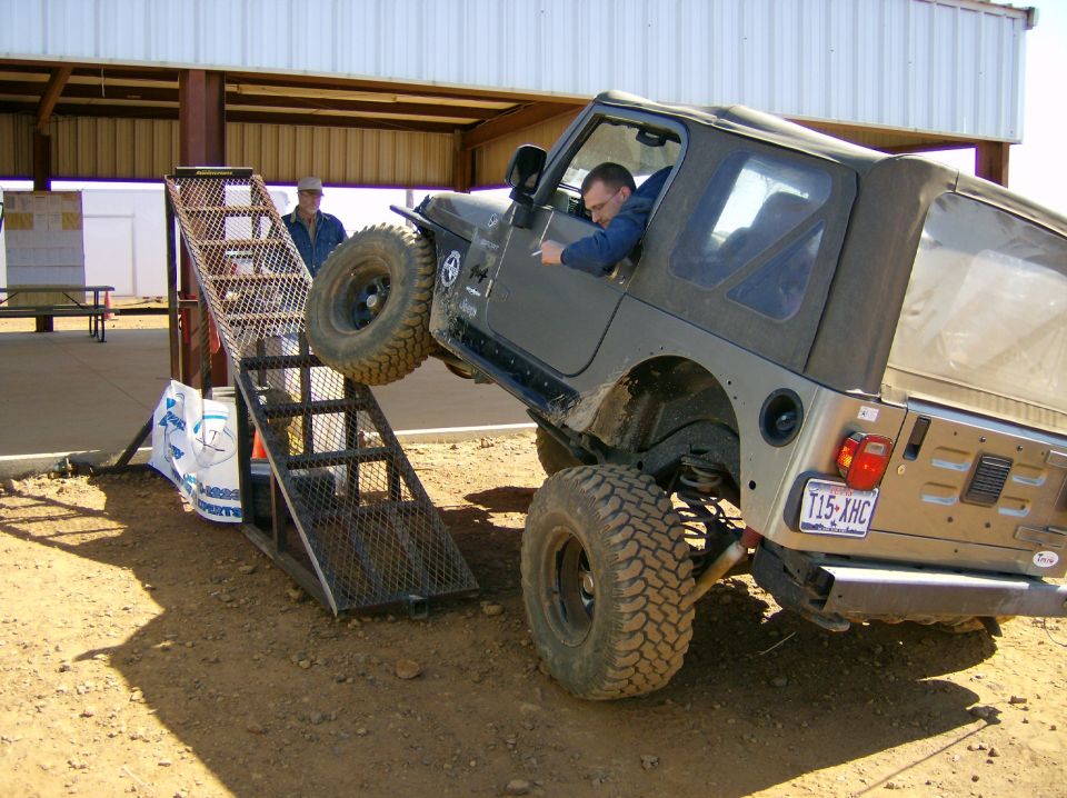 Jeep Wrangler driving up a metal ramp with a driver inside. License plate T15-AHC is visible
