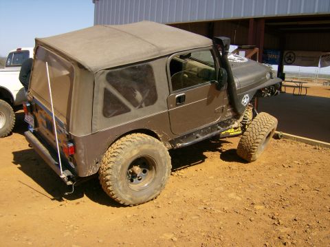 2004 Jeep Wrangler - A brown Jeep Wrangler with a soft top and snorkel is parked on a dirt lot next to a white truck.