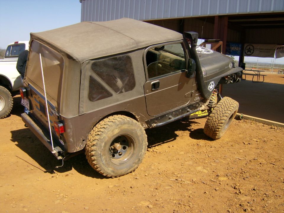 Brown Jeep Wrangler with soft top, snorkel, and large tires parked on dirt