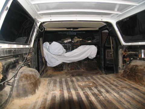 1978 Ford Bronco - The cargo area of a white SUV is shown, with a tarp-covered object obscuring the view of the rear seats.