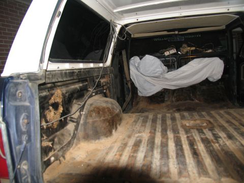 1978 Ford Bronco - The interior of a truck bed, covered in dirt and debris, with a tarped object inside.