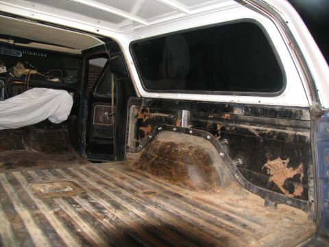 1978 Ford Bronco - The interior of an older SUV shows significant wear and tear, with rust visible on the wheel wells and a ribbed cargo floor.