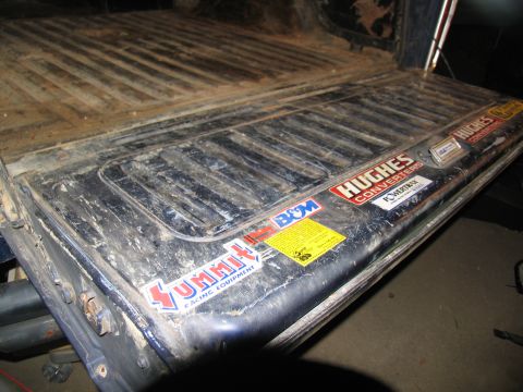 1978 Ford Bronco - A dirty black tailgate is covered in various racing and automotive stickers.
