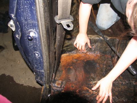1978 Ford Bronco - Interior of a blue vehicle showing extensive rust on the floor as people clean it.
