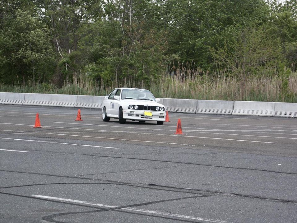 White BMW E30 M3 on a race track with orange cones, front view