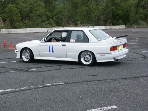 2001 Mercury Grand Marquis - A white BMW E30 M3 is seen on a race track with orange cones in the background.