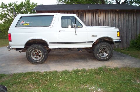 1988 Ford Bronco - This white Ford Bronco, likely from the late 1980s, is shown from the side with off-road tires and a lifted suspension.