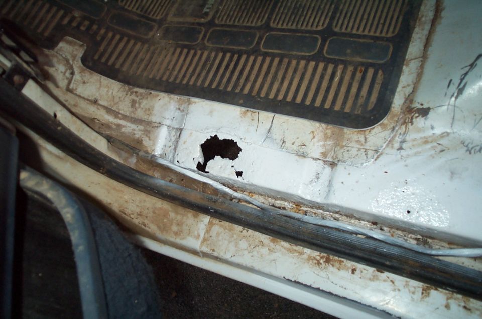 Rust hole in the white painted door sill and rocker panel of a truck cab