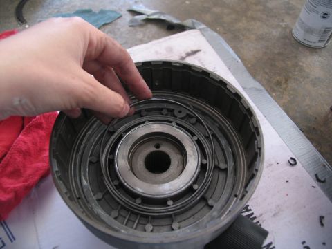 1978 Ford Bronco - A hand manipulates a thin metal ring within a complex transmission component during a rebuild.