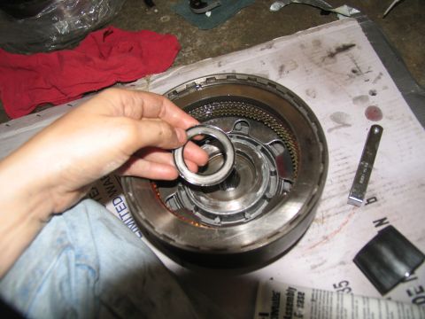 1978 Ford Bronco - A hand holds a transmission seal over the internal components of a transmission during a rebuild.