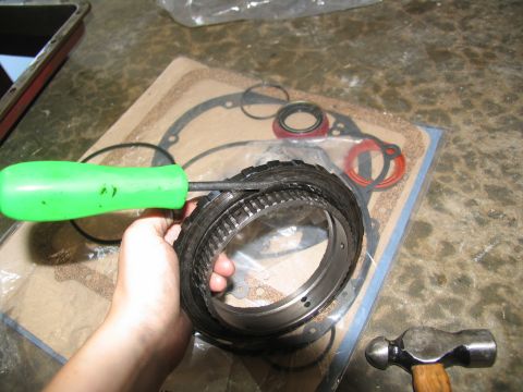 1978 Ford Bronco - A clutch pack from a transmission is being held with a green tool, with a gasket set and hammer nearby.