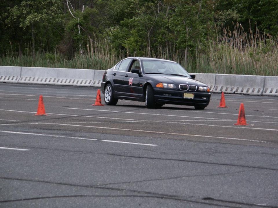 Black BMW 3 Series sedan with racing number 14 on the door, navigating an autocross course with orange cones