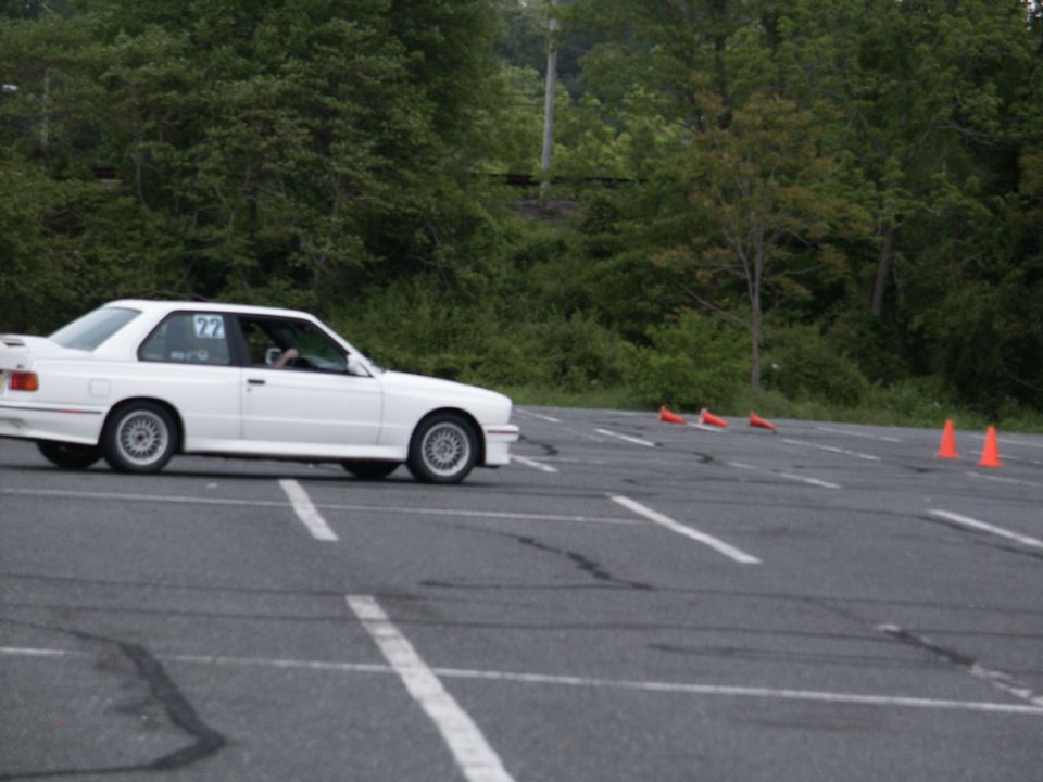 White BMW E30 M3 with racing number 27 on door, driving on an asphalt course with orange cones